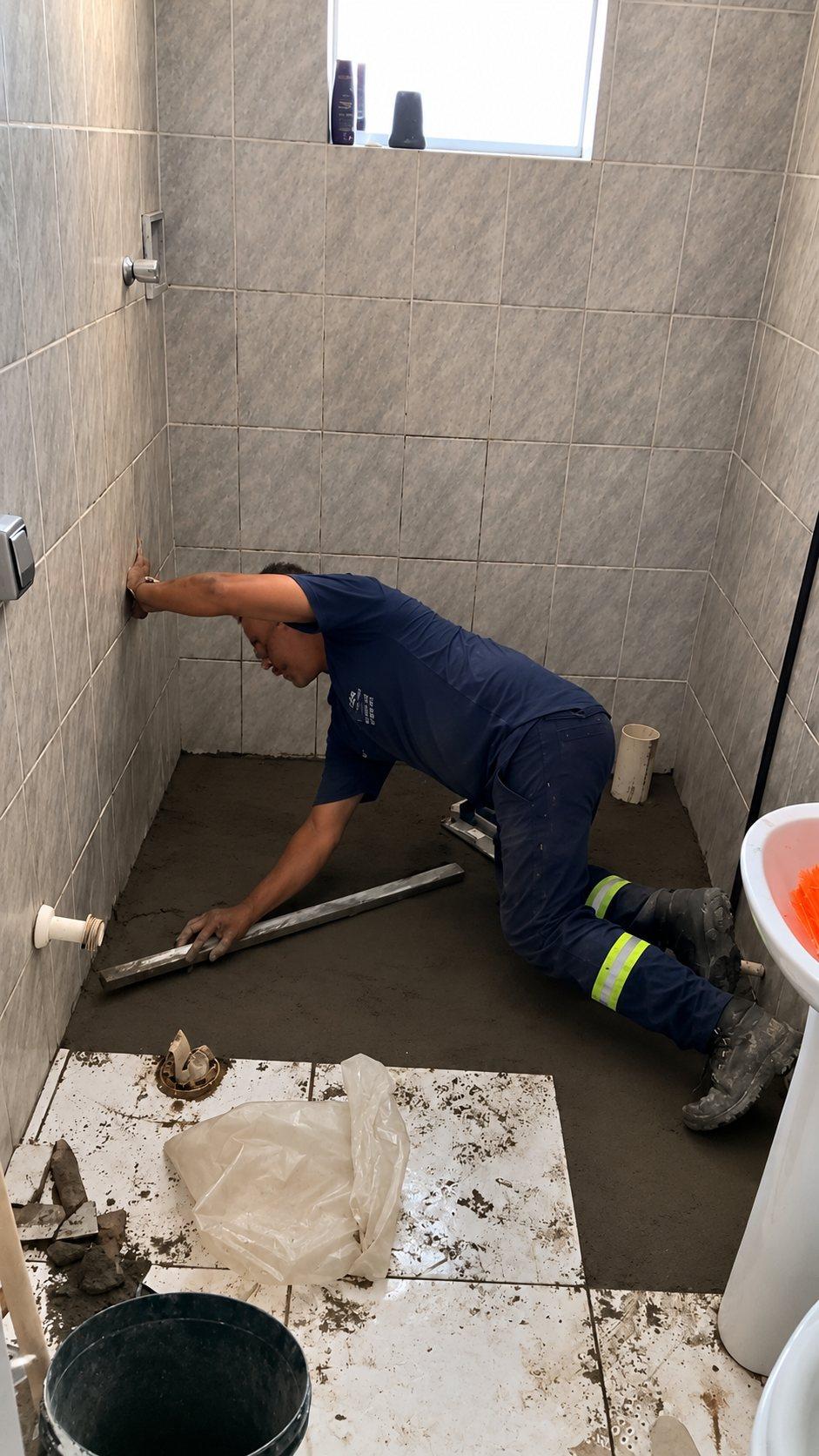 Profissional da MATECH regularizando com régua de alumínio o contrapiso de um banheiro de paredes revestidas